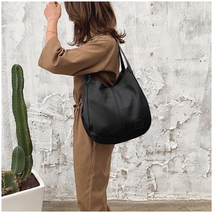 Detail of black large capacity hobo bag with textured leather and stitching shown on model