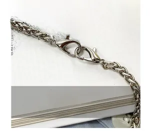 Dettaglio macro della catena in metallo argentato con chiusura a moschettone sulla borsa