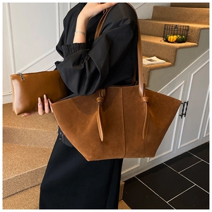 Detail view of brown suede wing tote bag and matching clutch set on shoulder of model