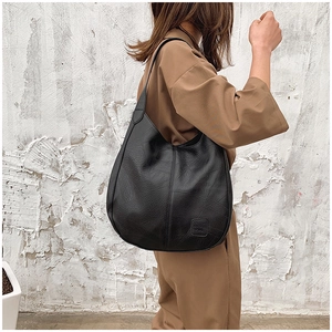 Close-up of a vintage black pebbled leather tote bag with a minimalist logo on a shoulder