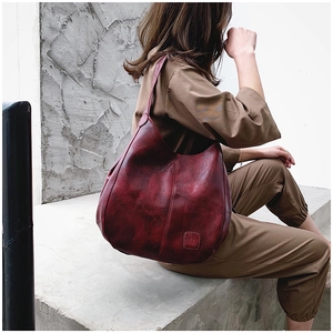 Detail view of burgundy soft leather tote bag with embossed logo and stitched texture