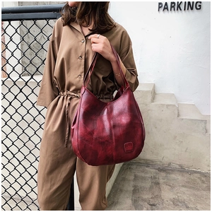 Detail of burgundy vintage textured tote bag carried on shoulder in outdoor street setting