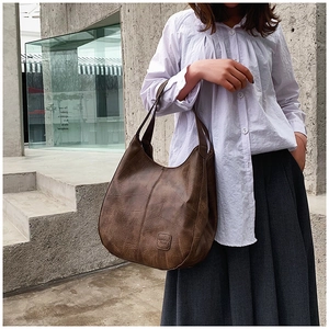 Detail view of the vintage brown leather texture and stitching on the large tote bag
