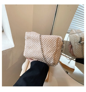 Detailed view of woven straw texture and silver chain strap on beige crossbody beach bag
