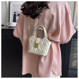 Detail of a creamy white quilted mini bag with gold chain strap and metal lock closure
