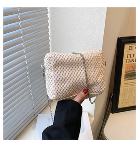 Detailed view of woven straw bag texture and silver metal chain strap on white purse
