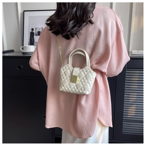 Detail of a beige quilted mini bag with a gold metal clasp and chain strap on a model