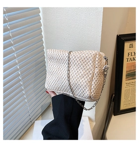Close-up of beige straw woven square bag with silver metal chain strap and zip closure