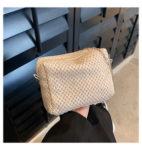 Detail of beige straw crossbody bag showing fine woven texture and silver metal chain