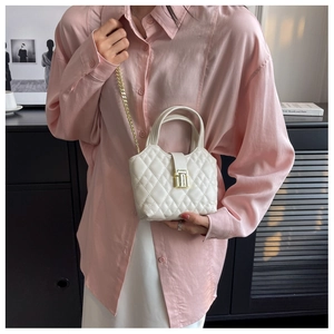 Detail of white quilted mini bucket bag with gold chain strap worn with a chic outfit
