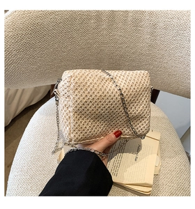 Detail shot of the beige straw woven crossbody bag with its elegant silver chain strap