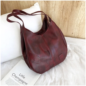 Detail view of burgundy soft leather hobo bag with pebble grain texture on white bedding