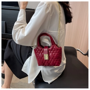 Detail of dark red quilted mini tote bag with gold chain strap on white shirt model