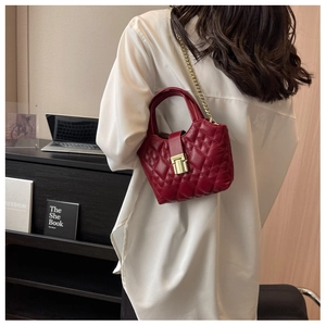 Close-up of wine red quilted handbag with gold lock and chain strap on a white shirt