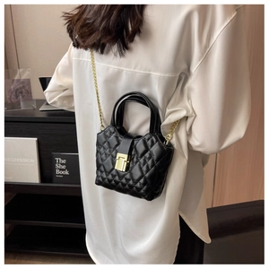 Detail of black quilted leather mini bag with gold chain strap worn as a crossbody