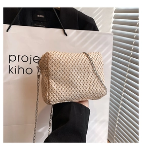 Detail shot of the beige straw woven texture and silver chain strap on the bag