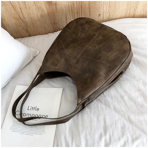 Detail of vintage brown textured leather hobo bag with patchwork design on white bedding