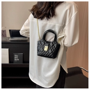 Detail of black quilted mini bucket bag with gold chain strap and twist-lock closure