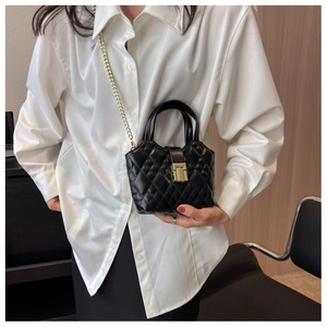 Fashionable black quilted mini bucket bag with gold chain strap shown on a white shirt