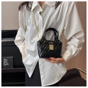 Close-up of a black quilted mini handbag with gold chain strap worn by a model