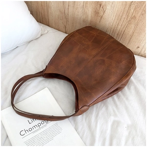 Detail of vintage brown leather hobo bag with unique stitching on a cozy bed background