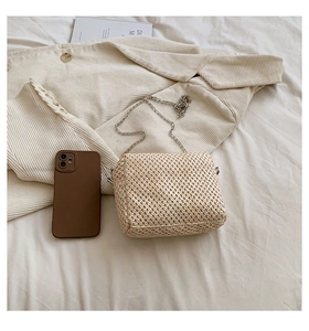 Straw woven crossbody bag in cream white with a slim silver metal chain on white sheets