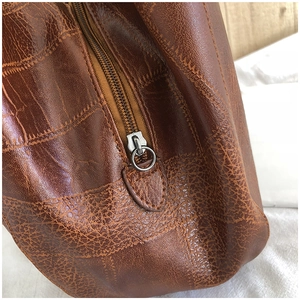 Detailed close-up of metallic zipper and cracked leather texture on brown tote bag