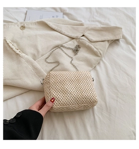 Detail of hand-woven straw crossbody bag with silver chain strap on soft fabric background