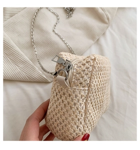 Detail view of woven straw crossbody bag with silver chain strap and metal zipper closure