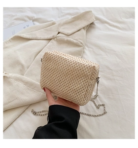 Detailed close-up of woven beige straw bag featuring a stylish silver metal chain strap