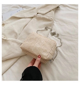 Detail shot of a cream woven straw crossbody bag with silver chain strap on beige fabric