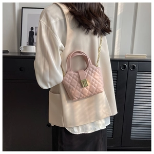 Detail of pink quilted mini bag with gold twist lock and chain strap on shoulder