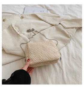 Close-up of beige woven straw crossbody bag with silver chain strap and zipper