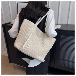 Détail du sac cabas tissé beige montrant la texture en V et l'étiquette logo en cuir