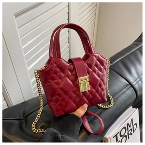 Detail of burgundy quilted mini bag with gold chain strap on a black leather sofa