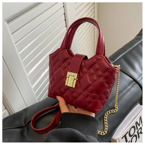 Detail shot of a dark red quilted leather bag with a gold metal lock and chain strap