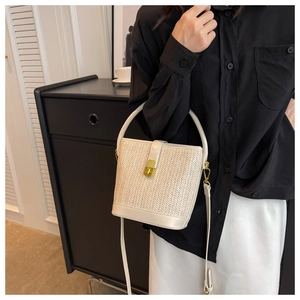 Detailed shot of white straw bucket bag featuring gold metal twist lock and leather trim