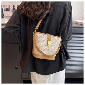 Detail of bohemian straw bucket bag showing gold twist lock and brown leather strap