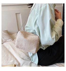 Detail of a minimalist beige woven crossbody bag with a slim silver chain strap