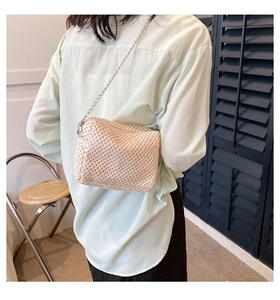 Detail of woven straw crossbody bag with silver chain strap shown on a model