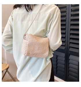 Detail of a creamy woven crossbody bag with a slim silver chain strap on a model