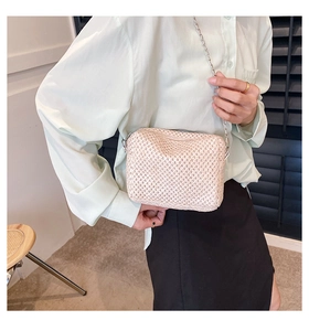 Detailed texture view of a beige straw woven crossbody bag with a silver chain strap