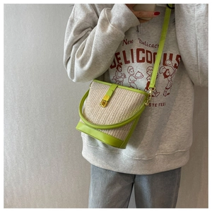 Detail of bohemian straw bucket bag with green leather trim and gold metal buckle
