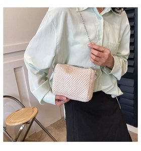 Detailed close-up of a woven straw crossbody bag with a delicate silver chain strap