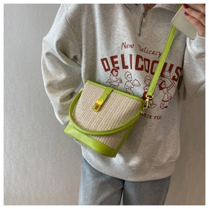 Close-up of woven straw bucket bag with light green leather trim and golden metal clasp