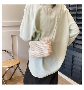 Fashionable beige straw crossbody bag with metal chain strap shown on a model