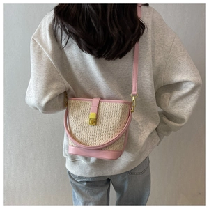 Detail of pink straw bucket bag with gold clasp shown on a crossbody model