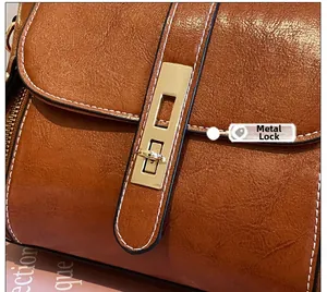 Dettaglio della chiusura dorata e cuciture bianche su borsa in pelle cerata marrone lucida