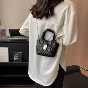 Chic black quilted mini crossbody bag with gold chain strap and handles worn by a model
