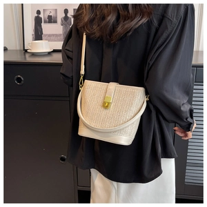 Detail view of woven straw bucket bag with gold metal twist lock and leather straps